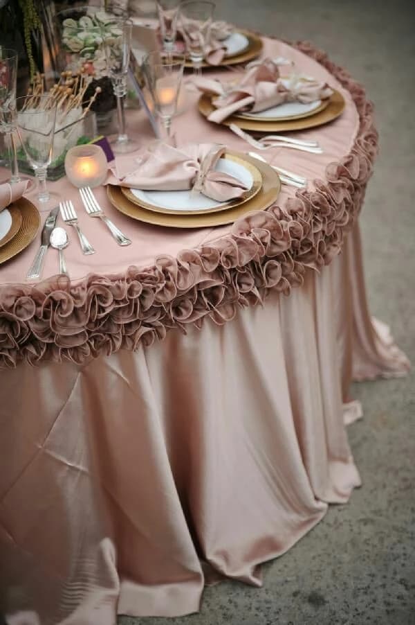 Table de réception ronde recouverte d'une nappe en satin vieux rose avec une large bordure florale à volants